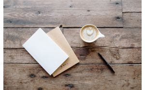 Notebook, coffee cup and pen on wooden surface
